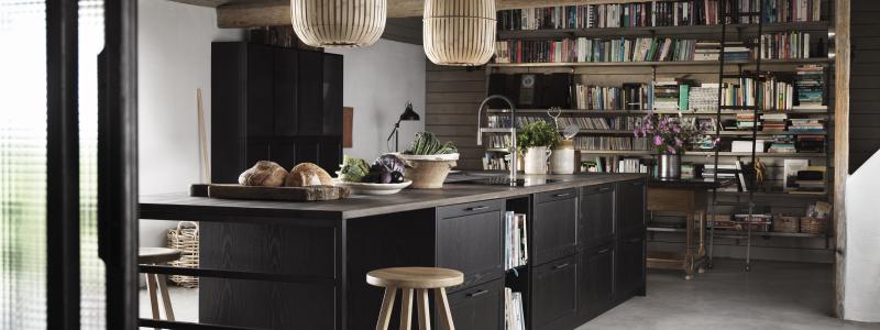 Ett kök att umgås i är svartbetsade Gastro från Ballingslöv. Luckor, lådor och bänkskiva i massiv ek. Den stora köksön rymmer alla kökets funktioner plus smart, luftig matplats. Trivsamt med böcker på väggen och tufft golv i slipad betong. Foto Ballingslöv