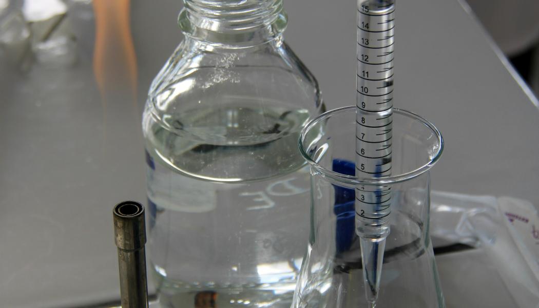En tekniker häller vätska i en Erlenmeyerkolv med en graderad pipett i ett laboratorieutrymme.  Genrebild: nathan rimoux/unsplash
