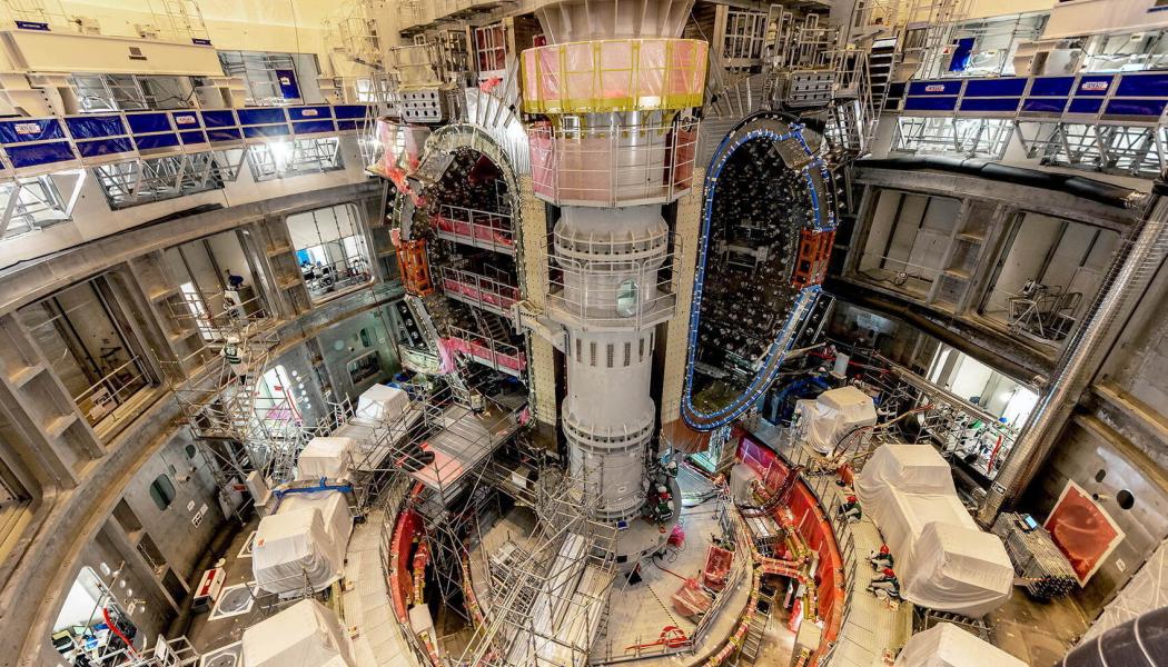  ITER-ingenjören Mathieu Demeyere övervakar lyftet tillsammans med säkerhetsansvarig Clément Vautrin från Framatome. – Den här vinkeln visar komponenterna i en sektormodul: vakuumkärlets 440-tonssektion, termiska skyddspaneler och ytan av en toroidmagnet. Foto: ITER
