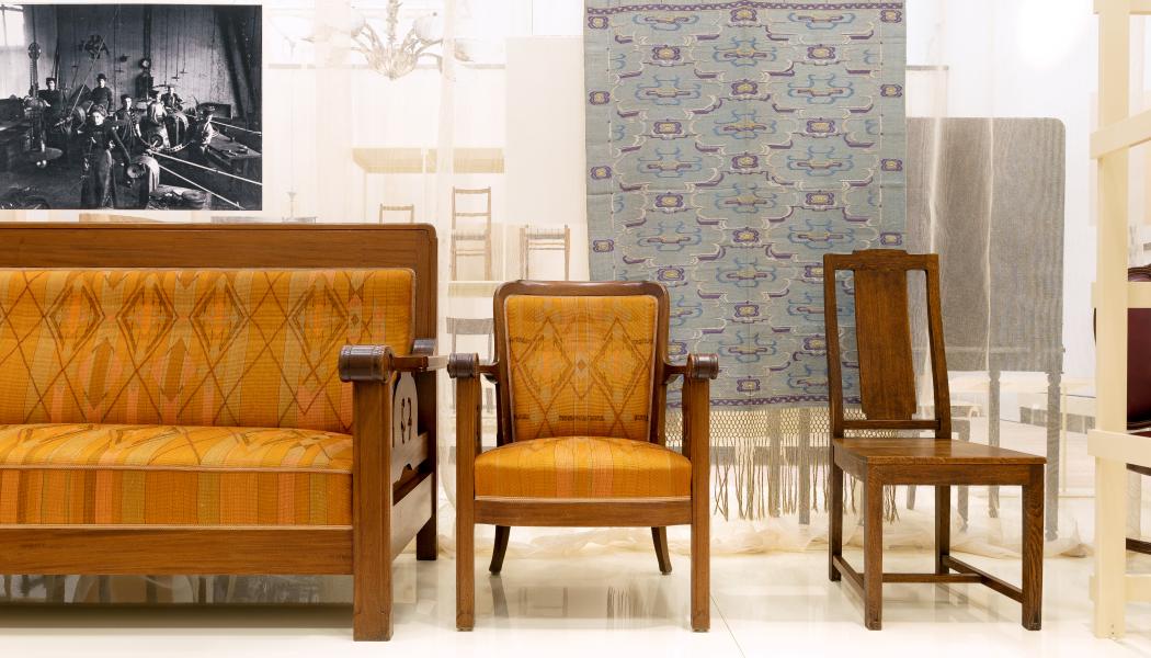 Möbler i jugendstil från verkstädernas tidiga år, kring 1910. Soffan och fåtöljen ritades av NK:s chefsarkitekt David Blomberg och stolen av Carl Westman, för Nyköpings tingshus. Textilier har alltid funnits med i NK:s utställningar och i de uppbyggda miljöerna på varuhuset. Gardinlängden är från Thyra Grafströms textilateljé, för en NK-miljö på Baltiska utställningen i Malmö 1914. Foto: Björn Dahlgren/Sörmlands museum
